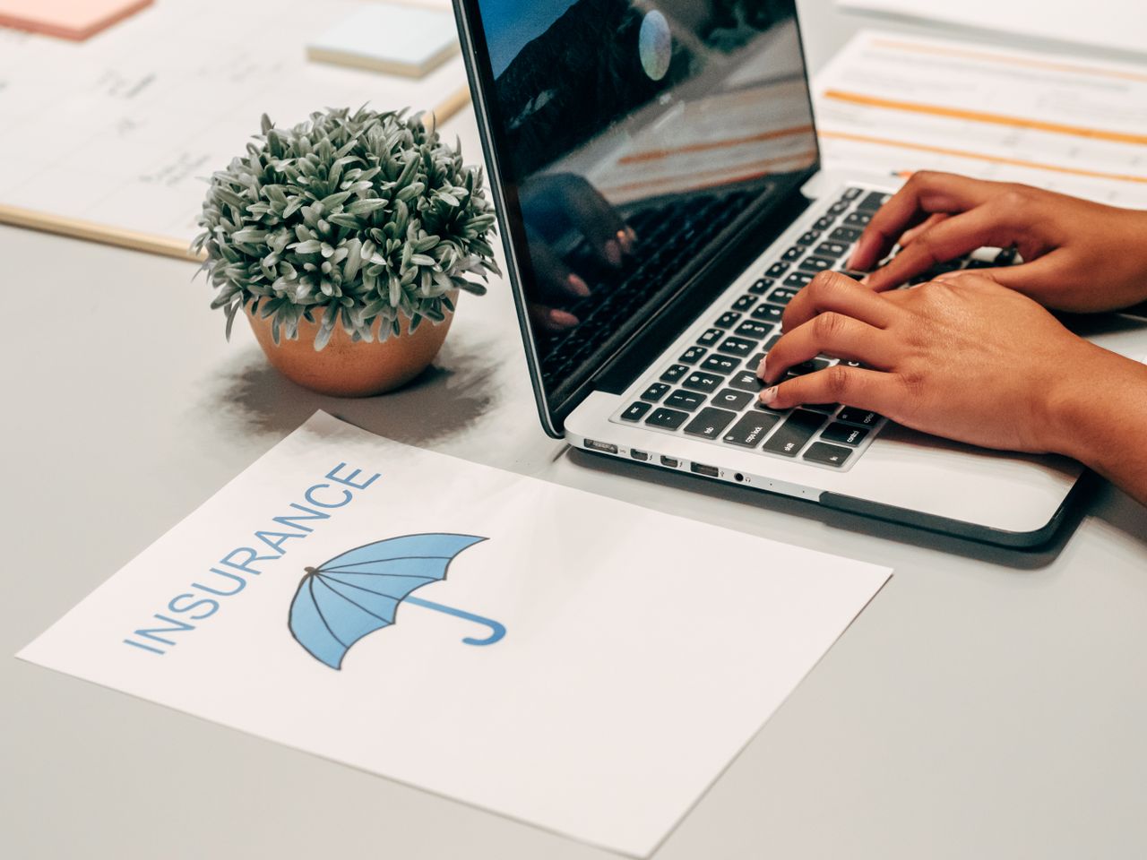 Crafting Captivating Headlines: Your awesome post title goes here Hands typing on a laptop at a desk with an insurance paper and plant, suggesting a work environment.